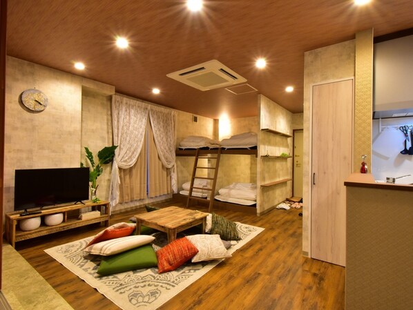 A compact hotel room with bunk beds, a TV, a wooden coffee table, and a small kitchen area.