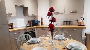 A modern kitchen with a wooden dining table set for four, equipped with white plates, glasses, and cutlery. - River views By Royal William Yard (Plymouth)