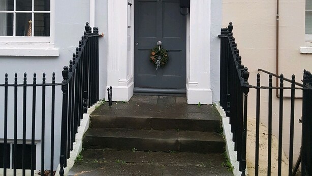 A two-story building with a dark grey front door, white trim, and a small wreath above the door. There are black iron railings on both sides of the front steps. - River views By Royal William Yard (Plymouth)