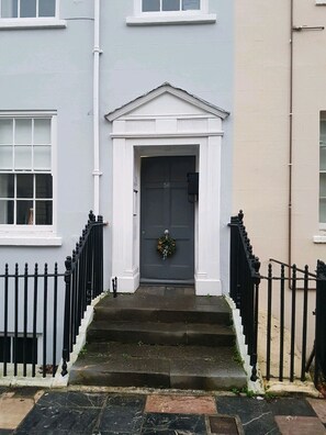 A two-story building with a dark grey front door, white trim, and a small wreath above the door. There are black iron railings on both sides of the front steps. - River views By Royal William Yard (Plymouth)