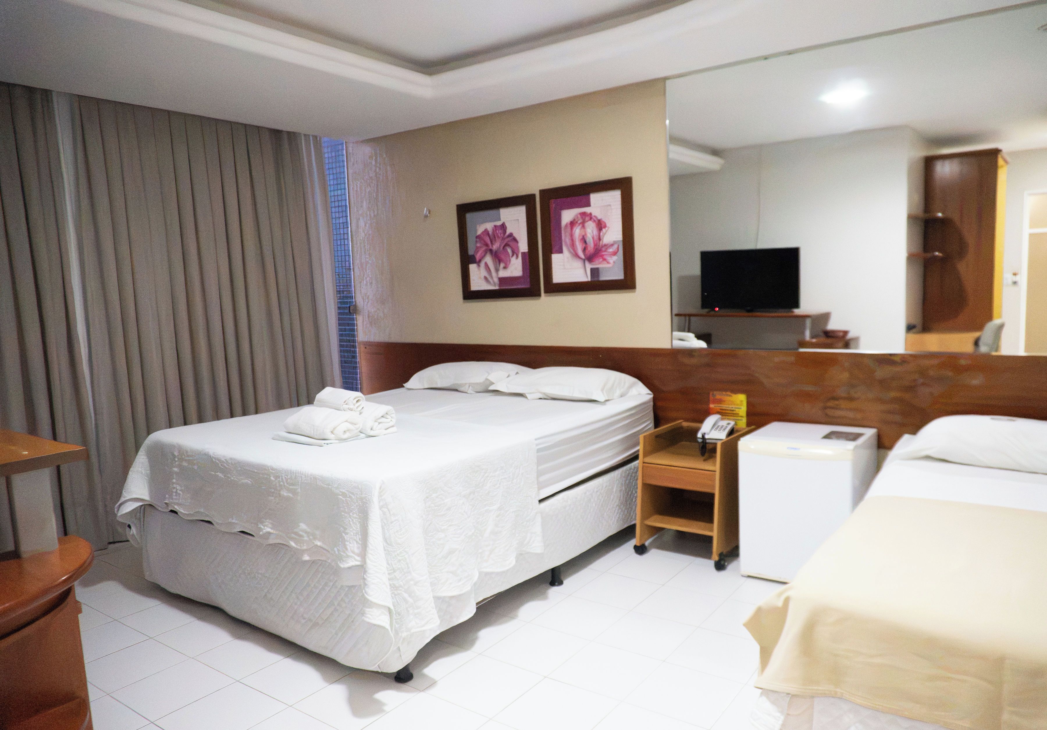 Una habitación de hotel con cama, mesita de noche, teléfono, televisión y espejo.