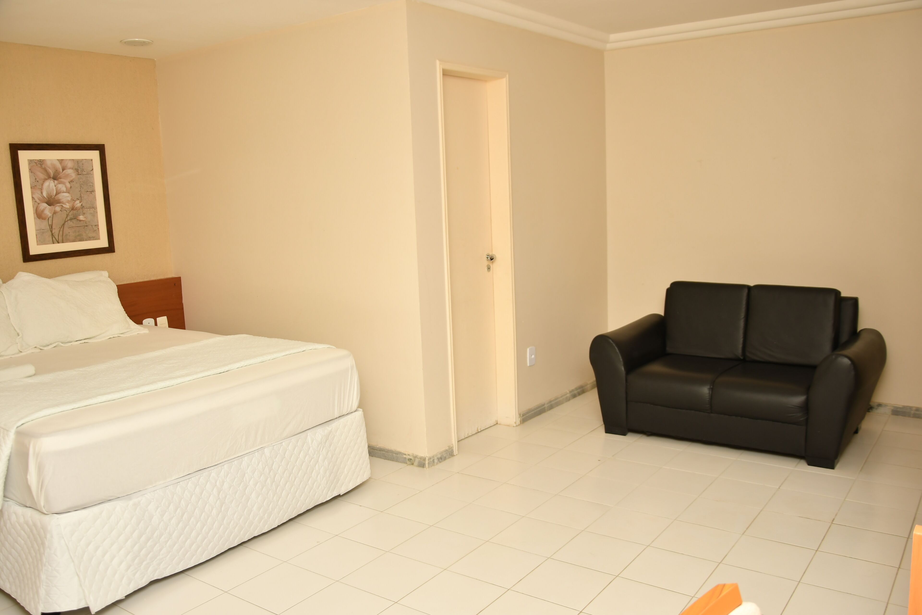 A hotel room with a bed, a black leather sofa, and a door leading to another room.
