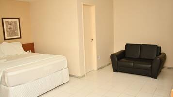A hotel room with a bed, a black leather sofa, and a door leading to another room.