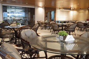 A restaurant with wicker chairs and a glass table, a bar with bottles in the background, and a sign with the number 09. - Troodon Park Hotel (Sousa)
