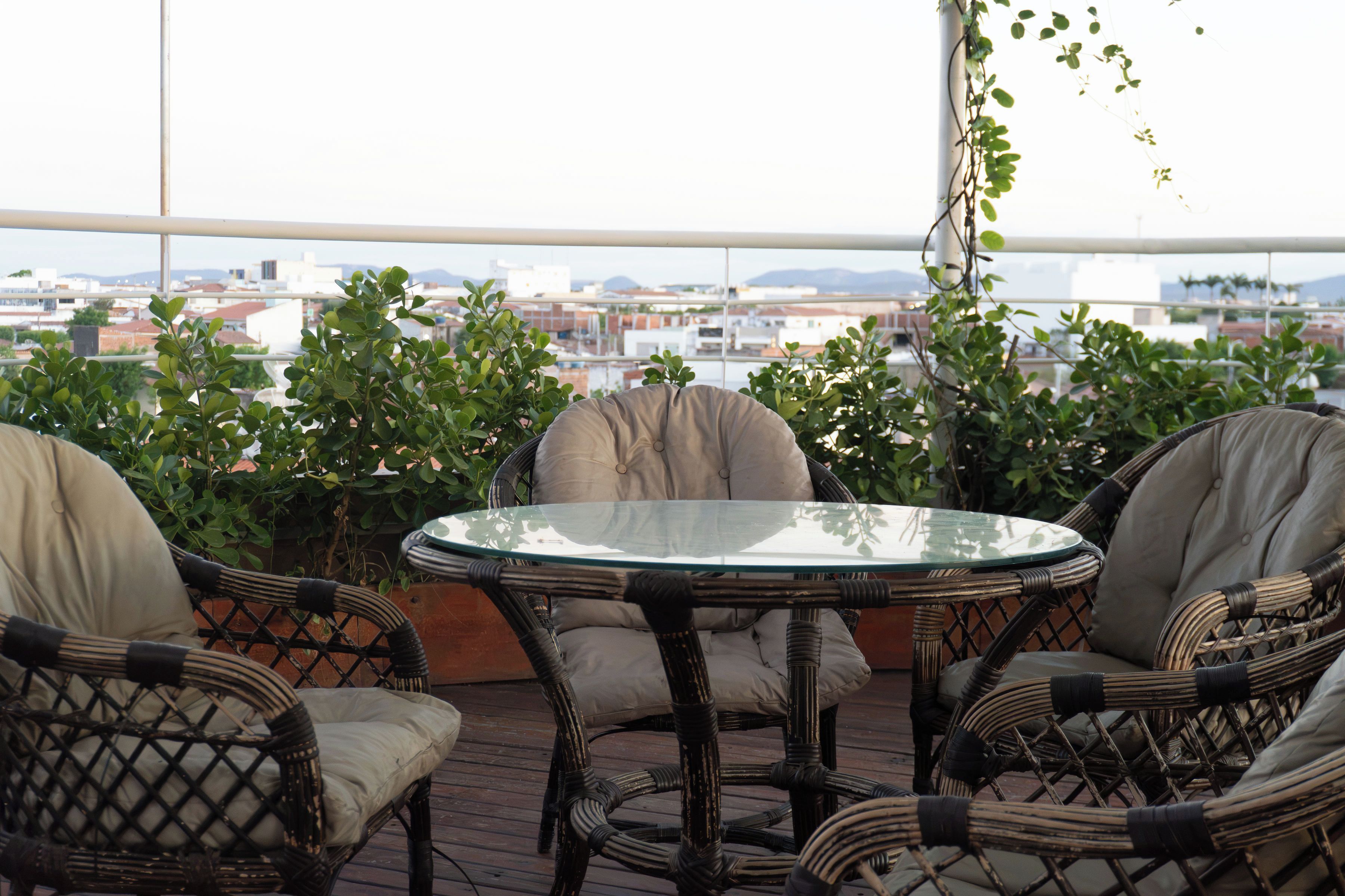 A balcony with wicker furniture and a glass table, overlooking a cityscape.