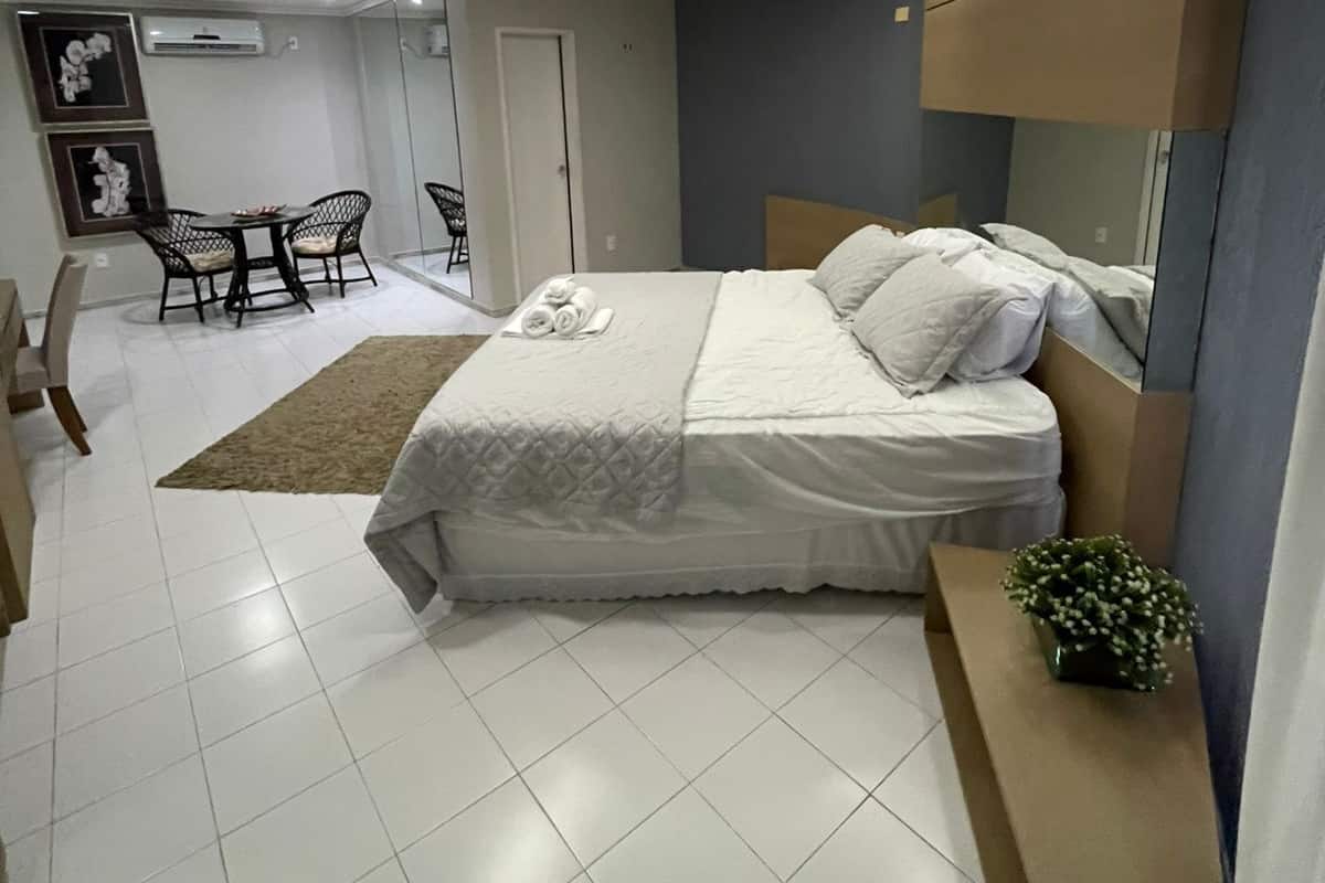 Un dormitorio moderno con una cama grande, una lámpara de techo circular, una mesita de noche con una planta y vistas al área de comedor.
