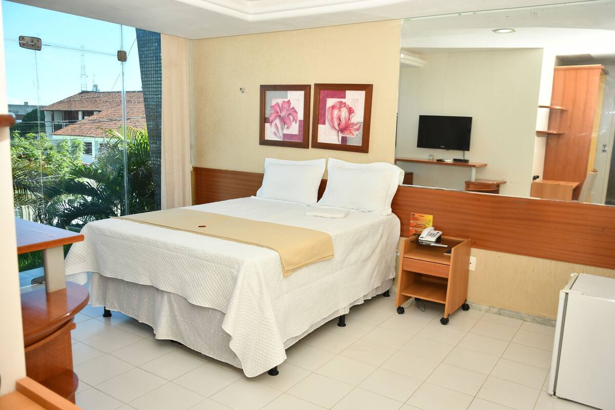 Una habitación de hotel con cama, escritorio, televisor y refrigerador.