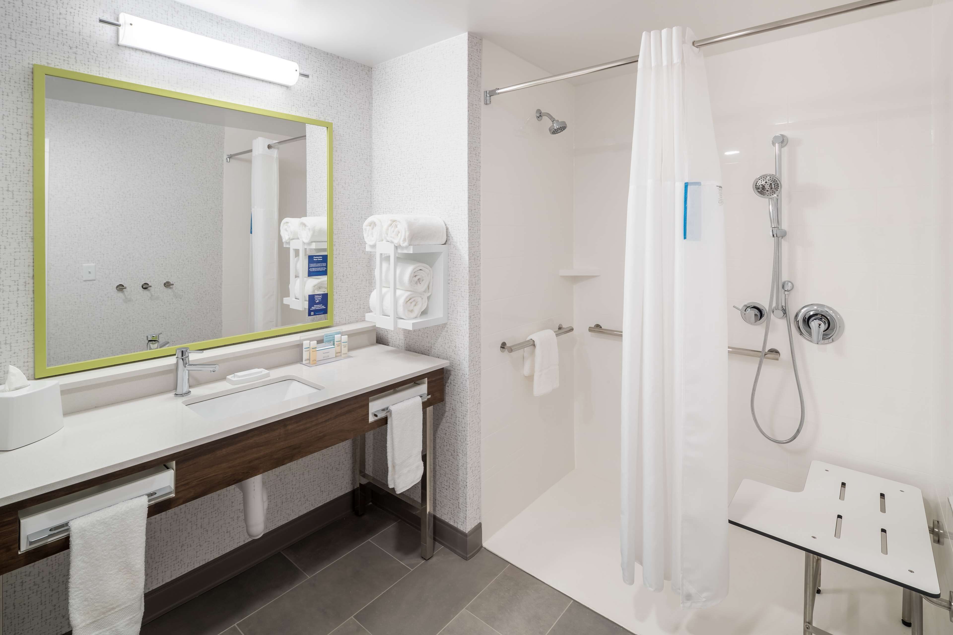 Un baño moderno con un espejo grande, ducha con puerta de cristal y lavamanos con toallero.