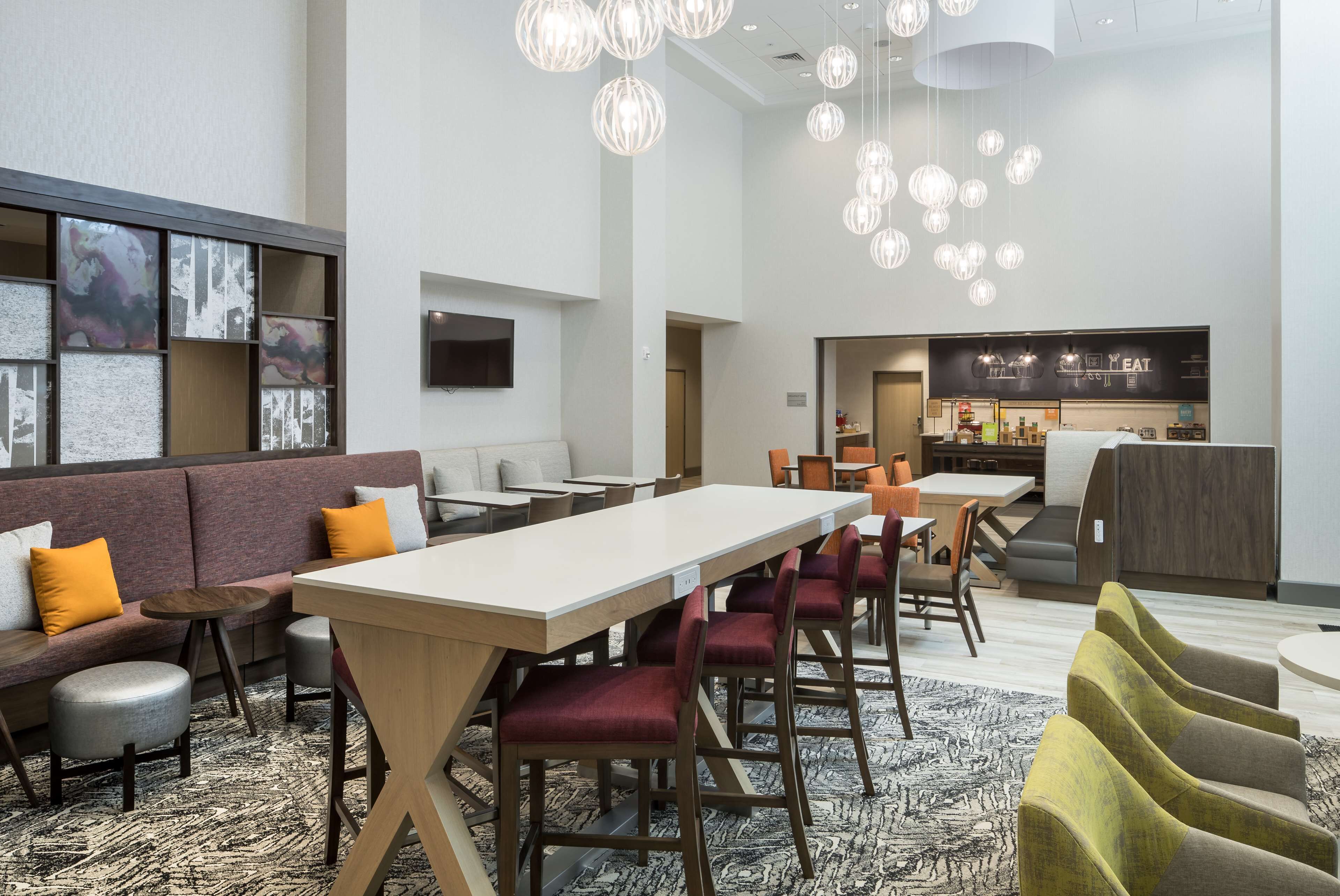 Un moderno vestíbulo de hotel con una larga mesa de comedor, asientos cómodos y una cocina al fondo.