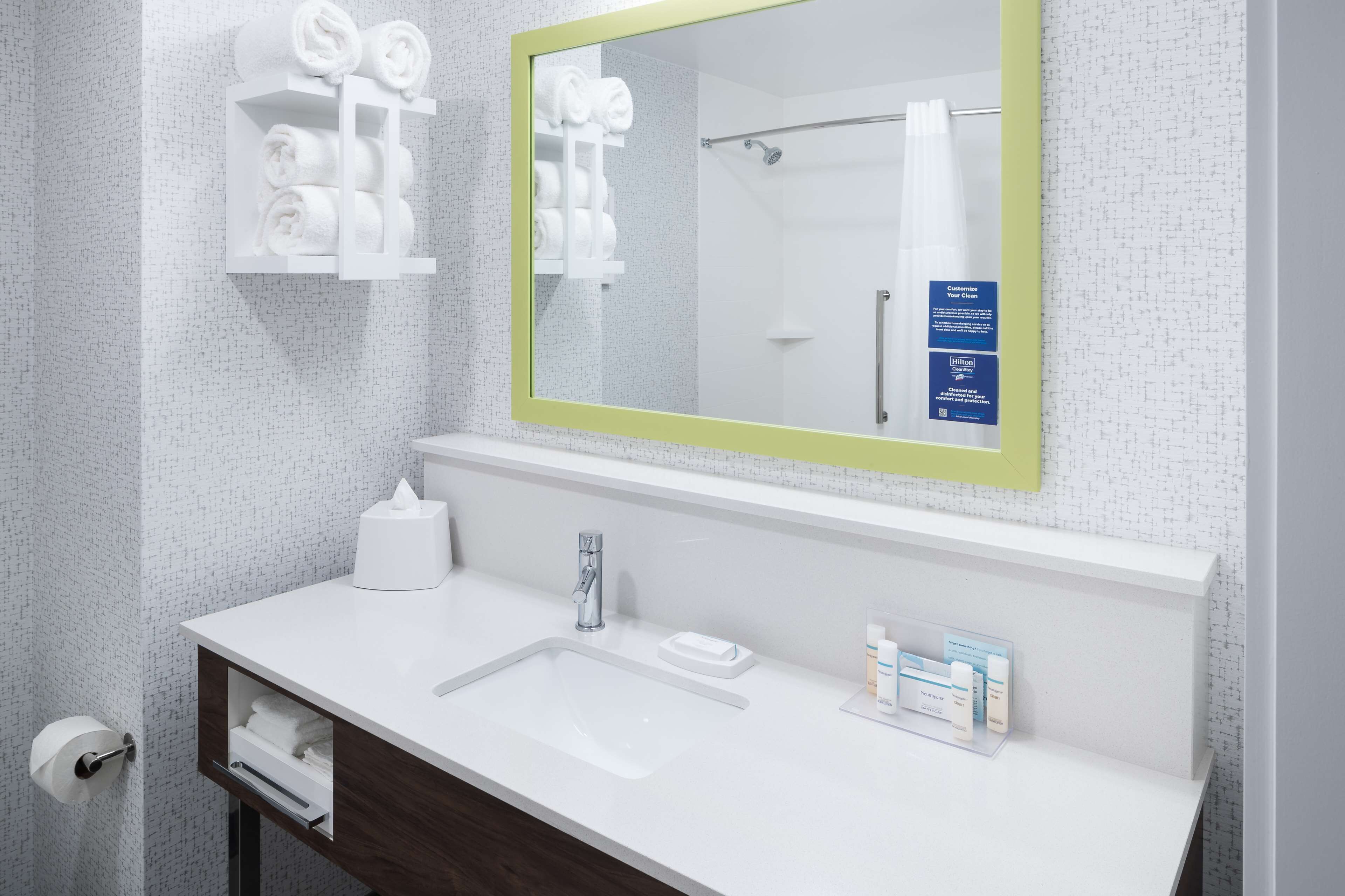 Un bagno moderno con un lavandino bianco, uno specchio con cornice verde e un portasciugamani con asciugamani piegati con cura.