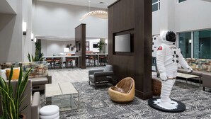 A modern hotel lobby with a seating area, a dining space, and a large screen.