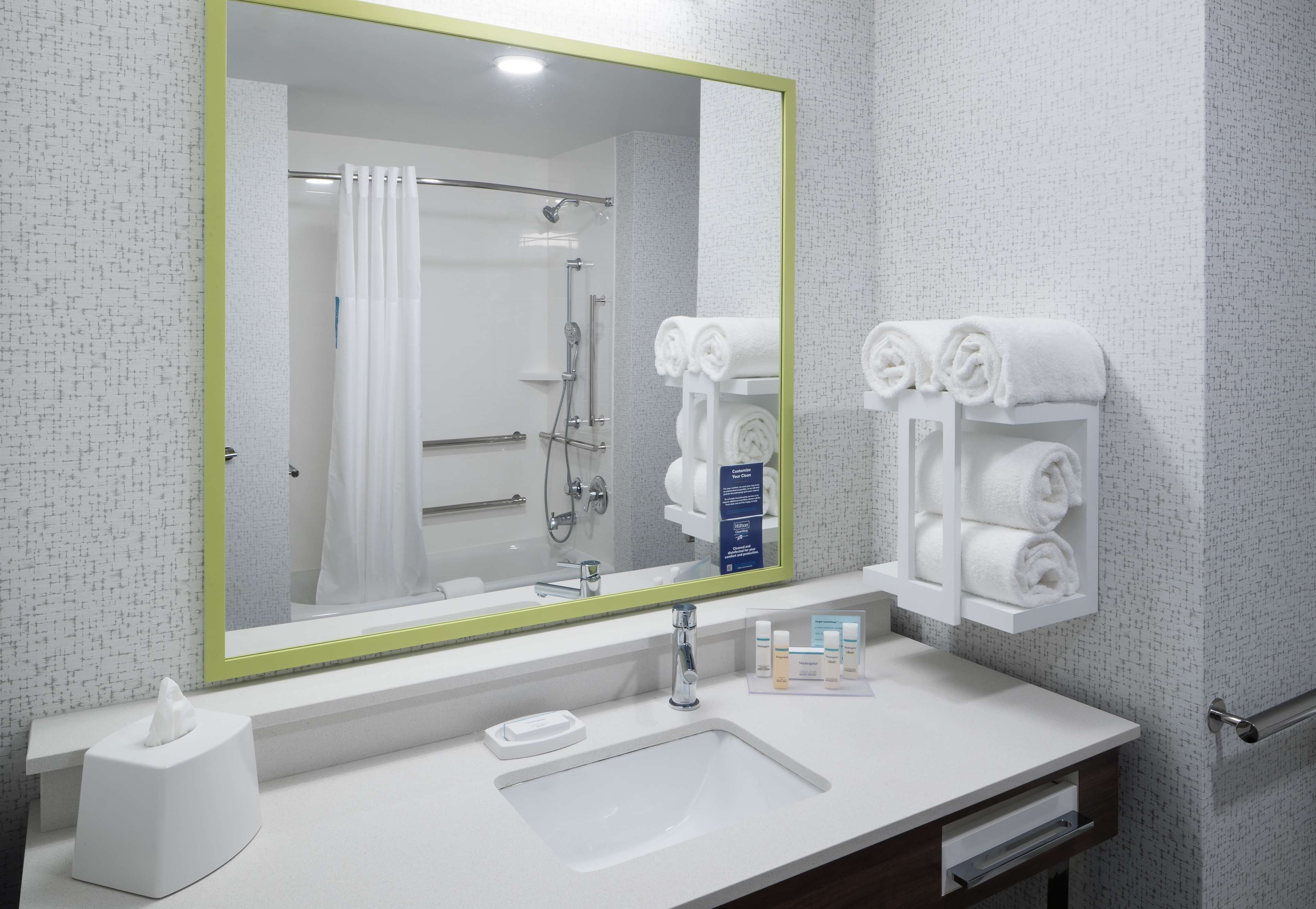 A modern bathroom with a large mirror, white sink, and towel rack.