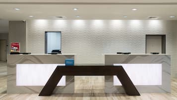 Un mostrador de recepción de hotel con diseño moderno, una pantalla digital y un letrero azul que indica el nombre del hotel.