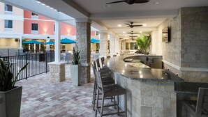 A spacious outdoor bar area with stone columns, multiple seating arrangements, and ceiling fans.