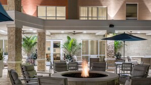 An outdoor seating area with a fire pit, surrounded by chairs and tables, in a courtyard with stone pillars and potted plants.