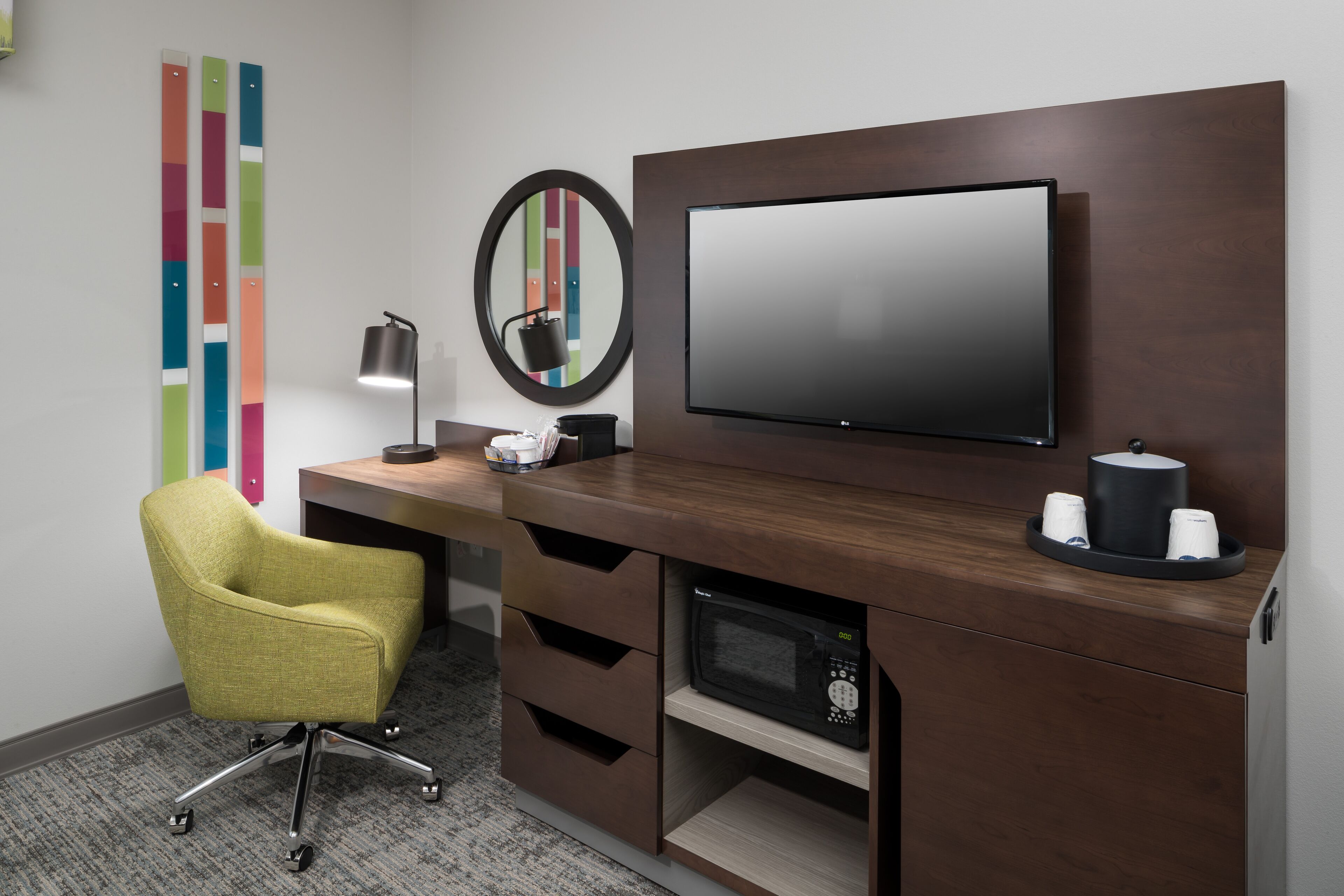 A modern office space with a desk, chair, flat-screen TV, microwave, and a coffee station.
