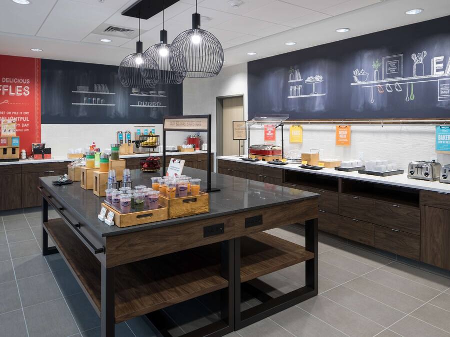 A modern kitchen area with a central island, various food items, and a chalkboard wall with the word "EAT".