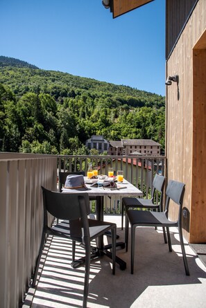 Un balcón con una mesa para dos, sillas y vistas a una colina boscosa.