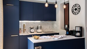 A modern kitchen with dark blue cabinets, a marble countertop, and a clock on the wall.