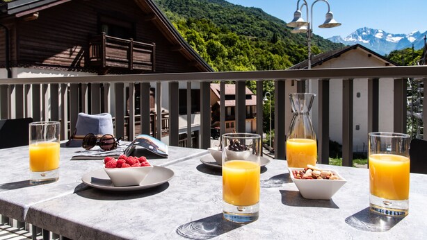 A table set with breakfast items including orange juice, a bowl of raspberries, and a plate of cereal, with a mountain view in the background.