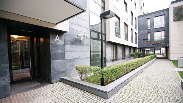 A modern building with a glass entrance, a well-maintained hedge, and a cobblestone pathway. - Warsaw Concierge Vistula Apartment (Warsaw)