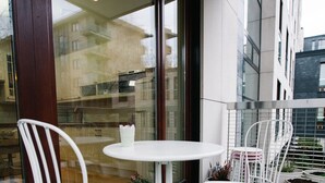 A balcony with white metal chairs and tables, potted plants, and a view of buildings through a glass door. - Warsaw Concierge Vistula Apartment (Warsaw)