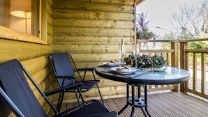 A wooden cabin with a round glass table and two black chairs on a deck. - Laurel Lodge - Log Cabin - St Florence (Tenby)