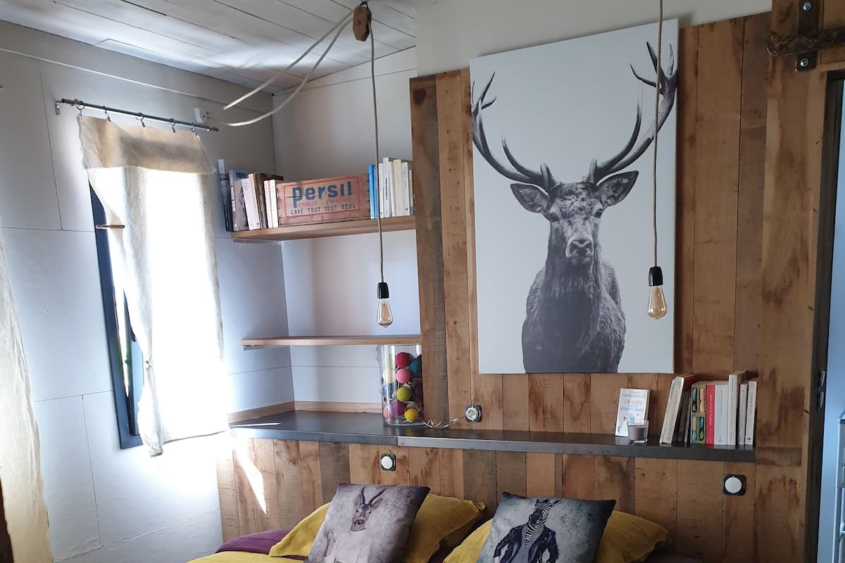 Un dormitorio con cama, almohadas, una colcha, estante con libros, una lámpara de pared y un cartel de un ciervo.
