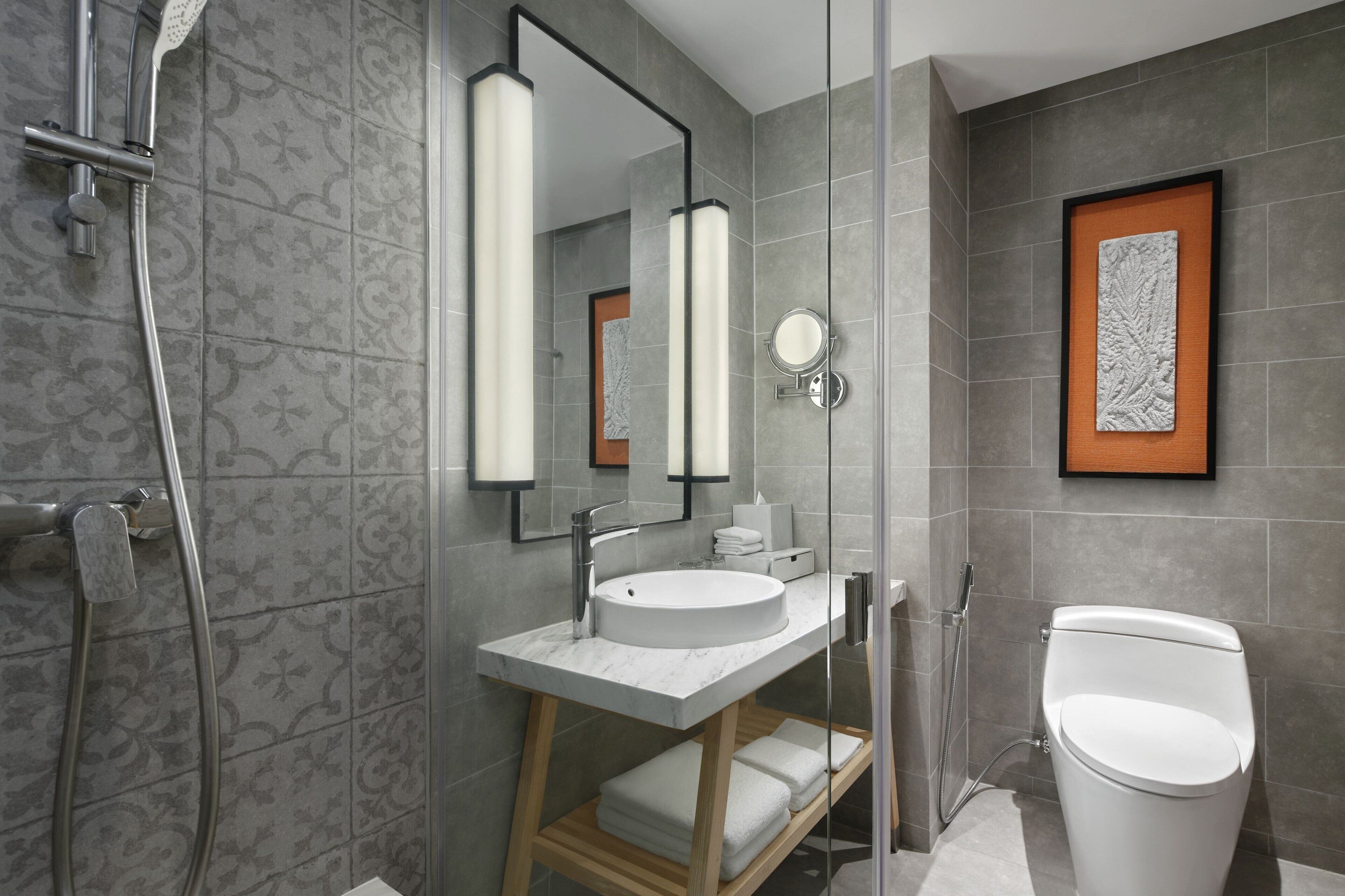 Un baño moderno con ducha envuelta en vidrio, un lavamanos blanco y un inodoro.