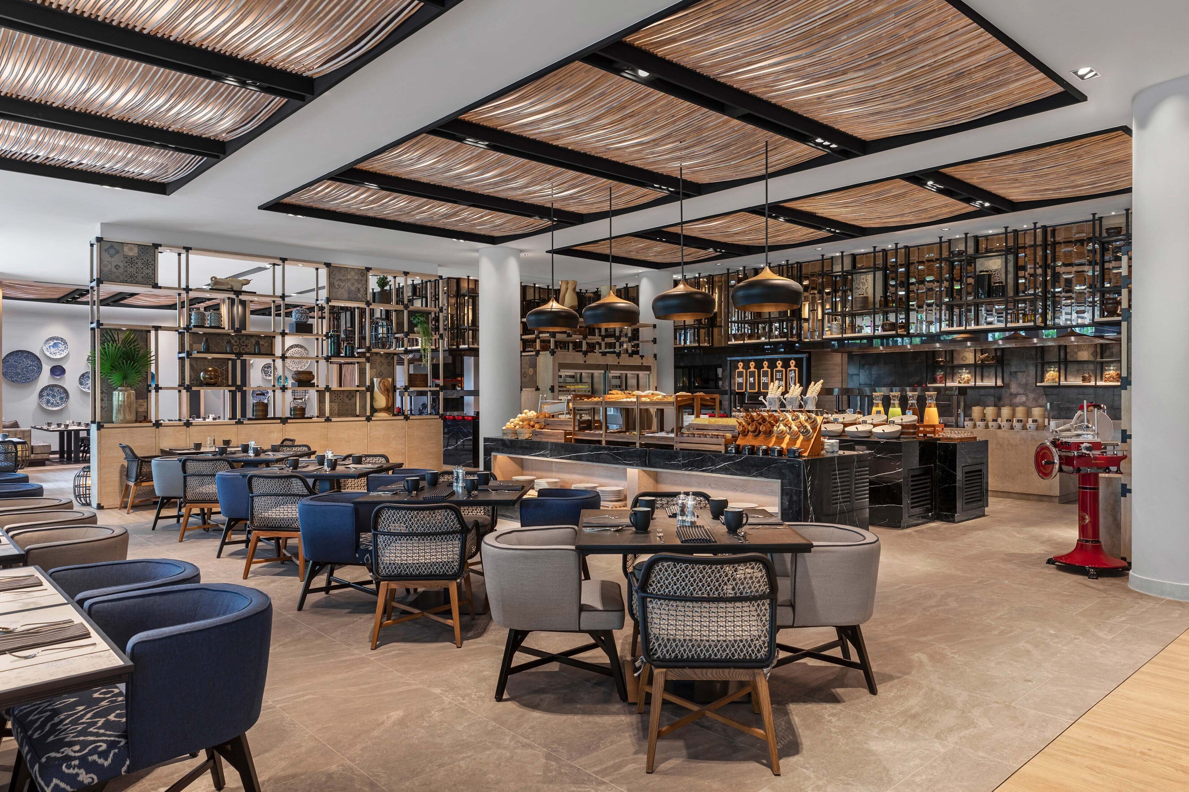 Ein modernes Restaurant mit hohen Decken, sichtbaren Holzbalken und verschiedenen Sitzgelegenheiten, darunter Tische und Stühle.