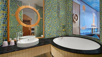 A bathroom with a large oval sink, a round mirror, and a shower. The walls are tiled with a mosaic pattern.