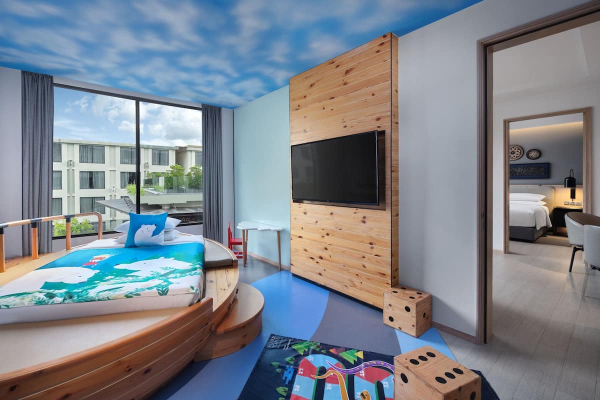 Habitació d'hotel moderna amb un llit gran, una televisió penjada en un panell de fusta, un balcó amb vistes a edificis i una petita zona de treball.