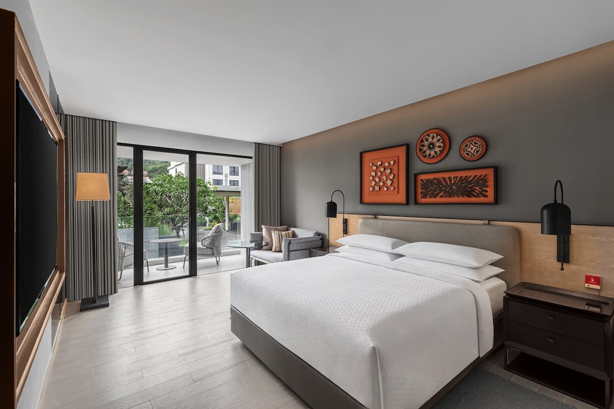Una habitació d'hotel moderna amb un llit gran, una taula de treball i un balcó amb mobles de jardí.