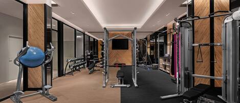 A modern gym with various exercise equipment, a bench, and a television screen on the wall.