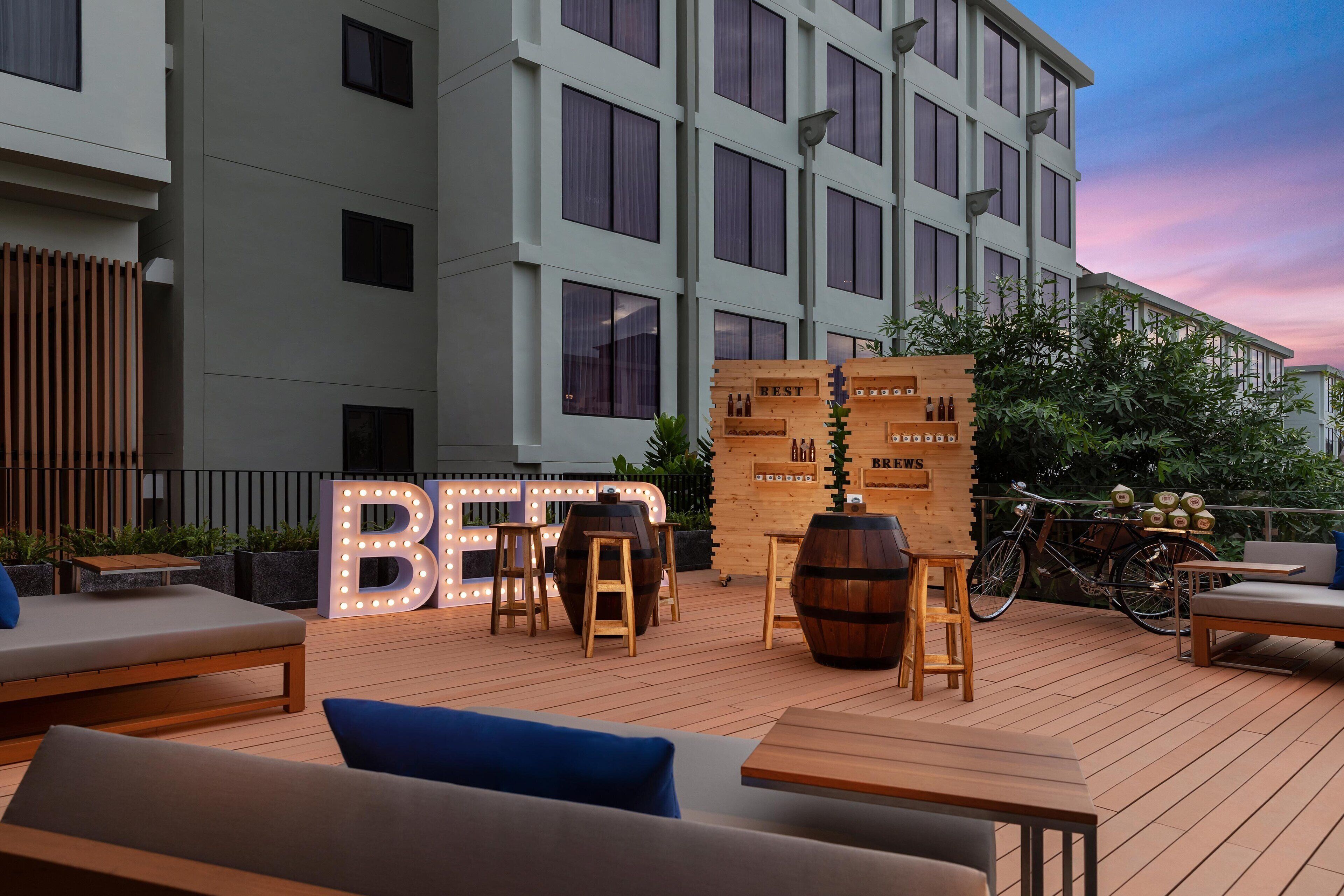 Un bar sul tetto con mobili in legno, grandi lettere illuminate con la scritta 'Brewery' e una bicicletta parcheggiata nelle vicinanze.