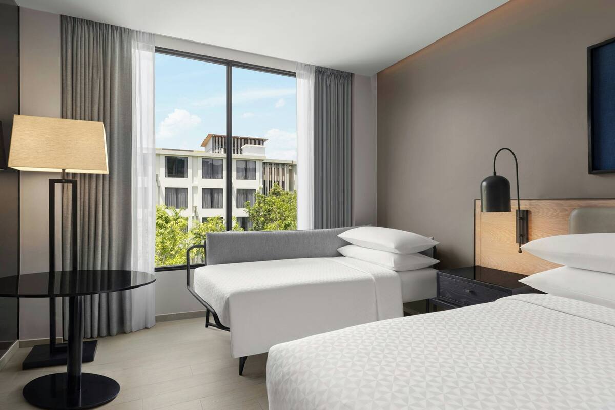 Una habitación de hotel moderna con un ventanal grande, una mesa redonda, una cama, una mesita de noche y una lámpara.