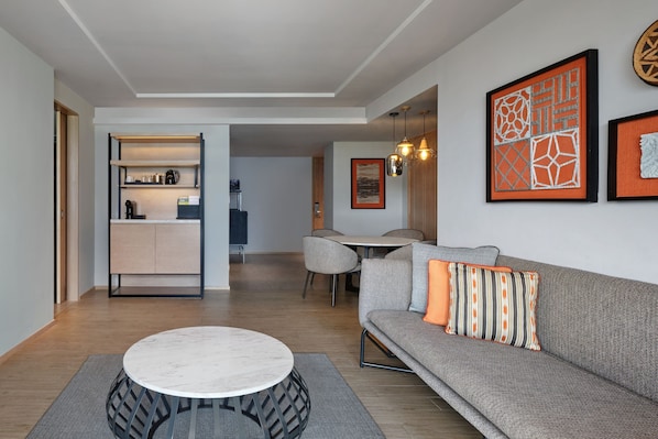 Una sala de estar moderna con un sofá gris, una mesa de centro redonda y un comedor con mesa y sillas.