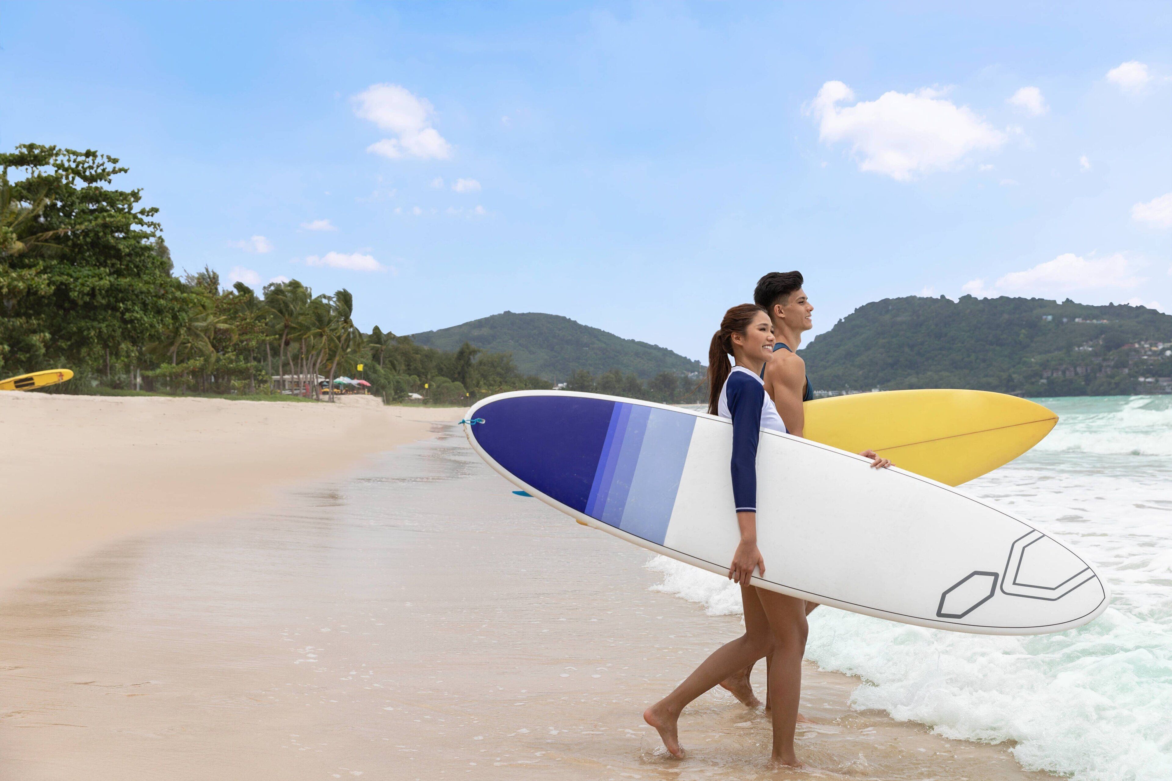 A beach scene with two people carrying surfboards.
