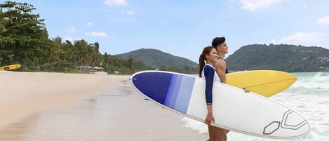 A beach scene with two people carrying surfboards.