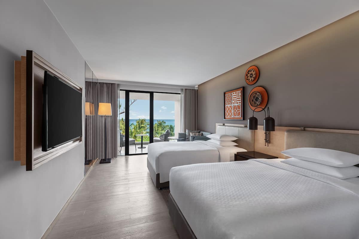 Habitació d'hotel moderna amb dos llits, televisió de pantalla plana, un balcó amb vista a l'oceà i zona de menjador amb taula i cadires.