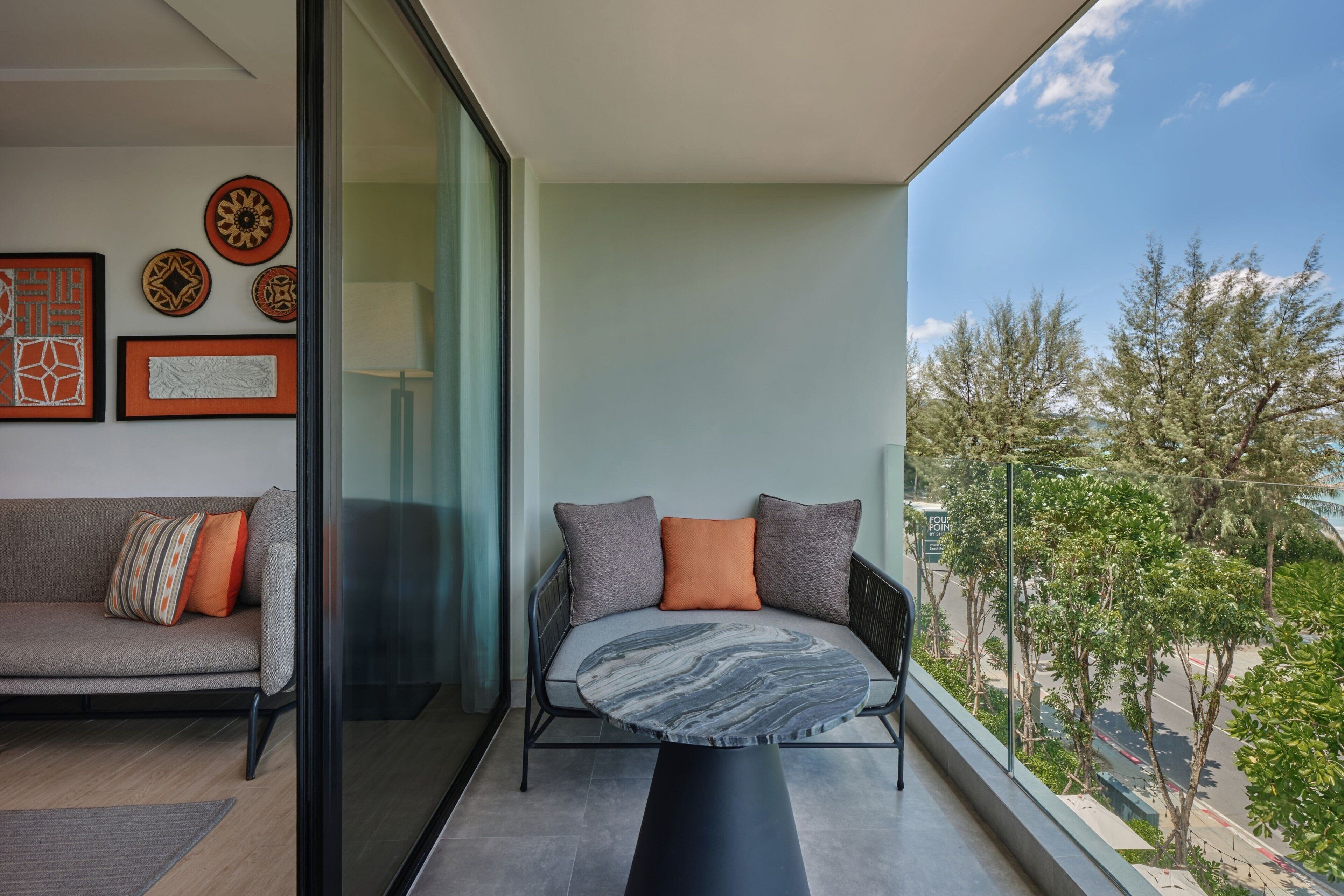 A balcony with a sofa and a round table, a city view, and framed artwork on the wall.