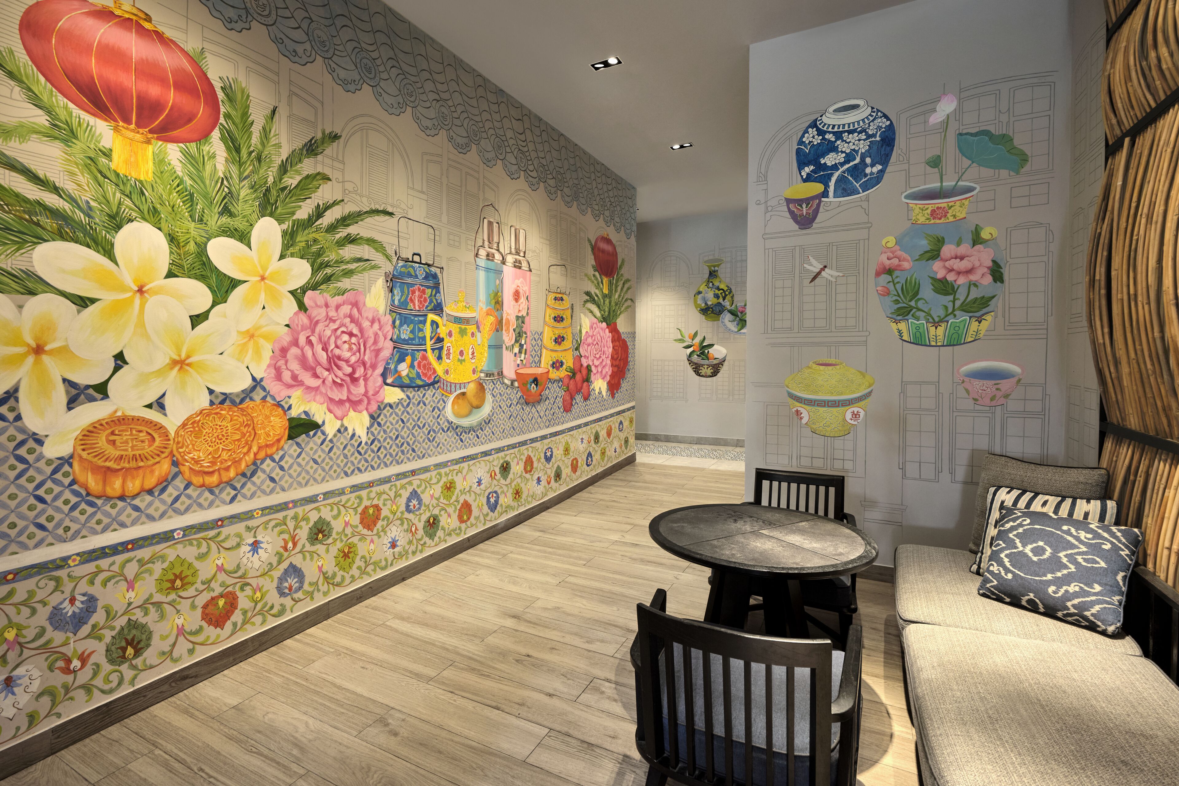 A room with a tiled wall featuring floral and traditional patterns, a round table with chairs, and a sofa with cushions.