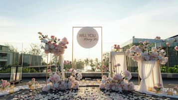 En bröllopsceremoni med en skylt där det står ”Vill du gifta dig med mig?”, blomsterarrangemang och en träveranda.