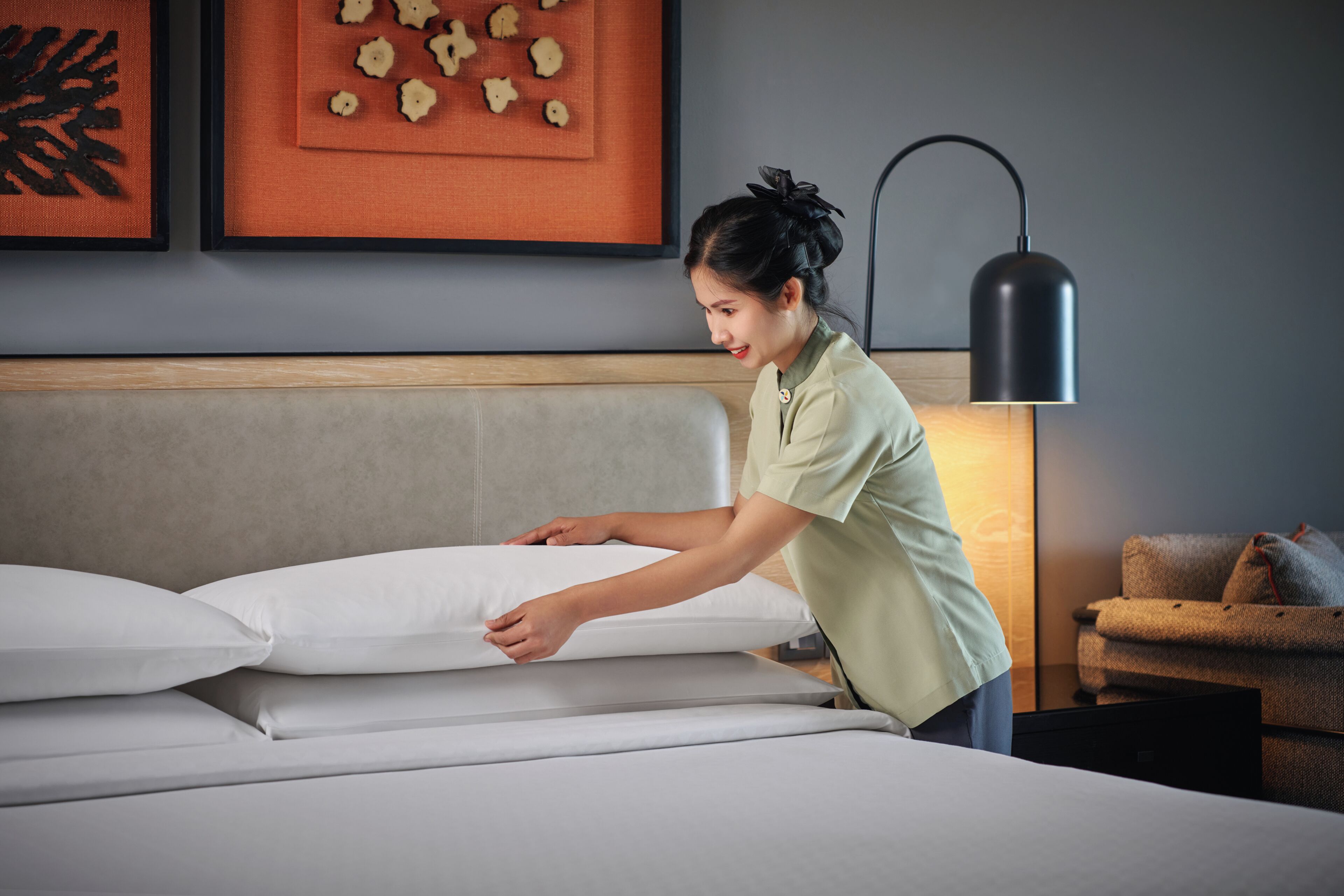 A person adjusting a bed in a hotel room with a modern design, including a headboard and wall art.