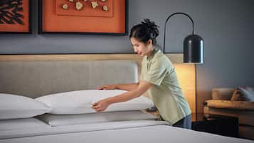 A person adjusting a bed in a hotel room with a modern design, including a headboard and wall art.