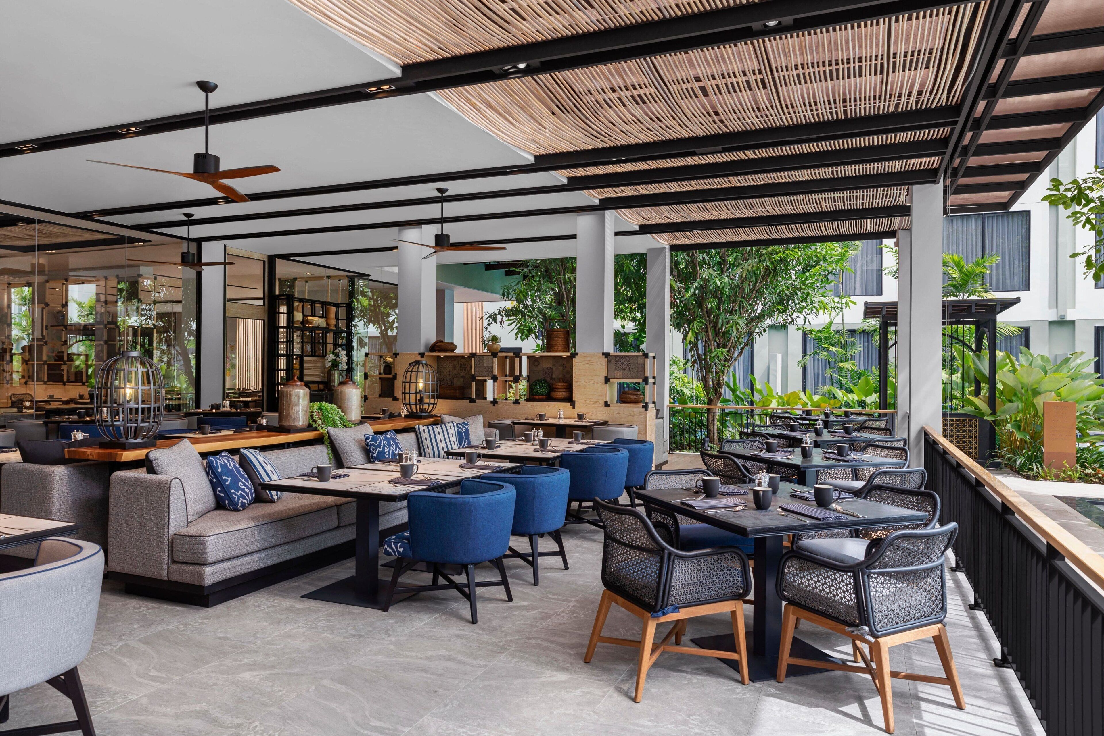 A modern restaurant with indoor and outdoor seating, large windows, and a ceiling fan.