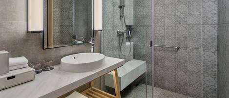A modern bathroom with a large mirror, a round sink, a glass shower enclosure, and a wooden shelf with towels.