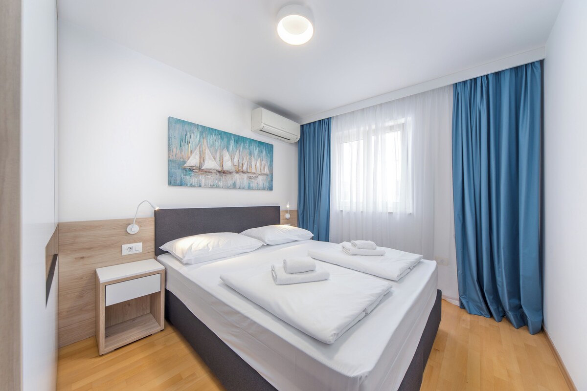 Quarto de hotel com cama, mesa de cabeceira, um quadro e janela com cortinas.