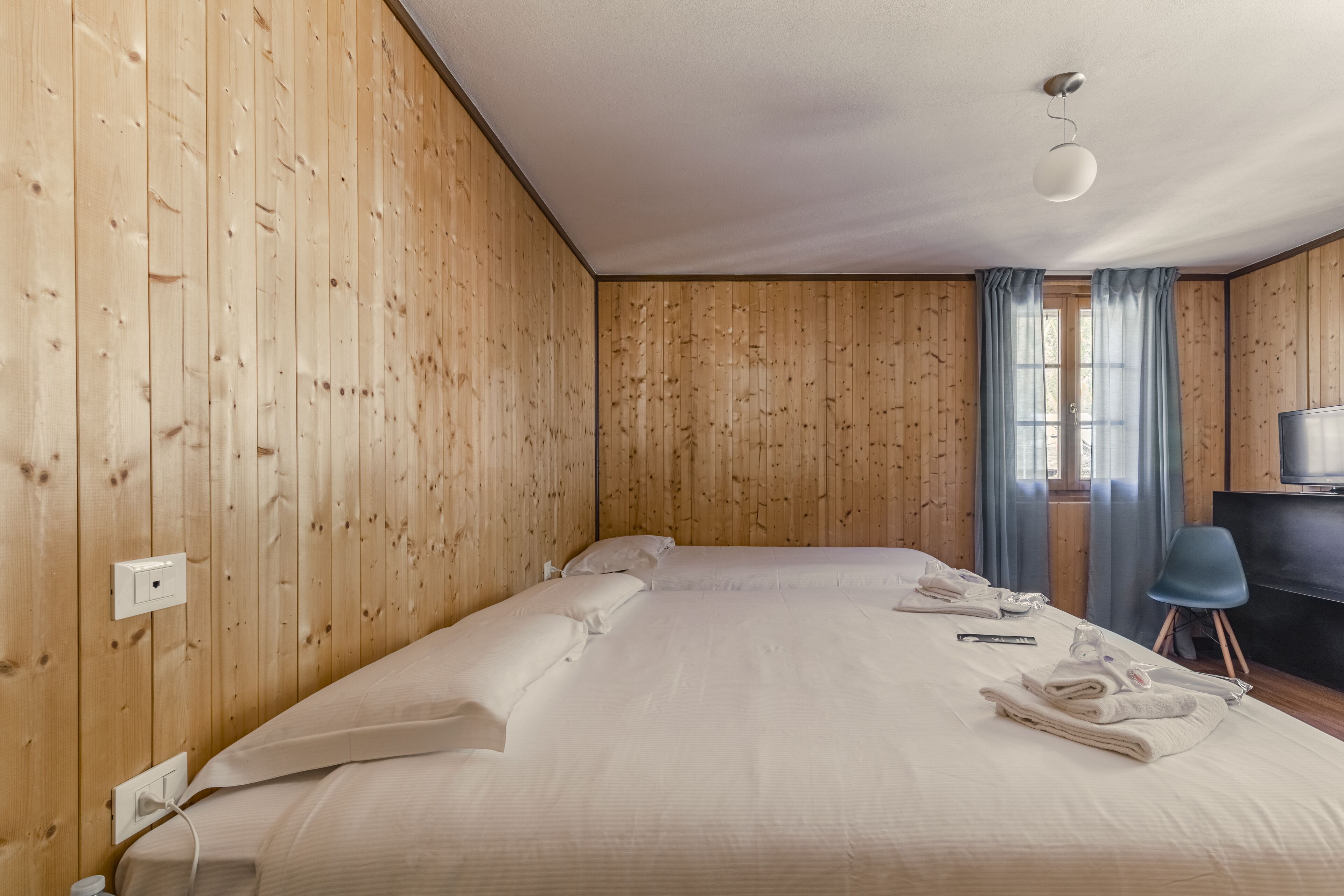 A hotel room with wooden panel walls, a large bed with white linens, a desk with a chair, and a television.