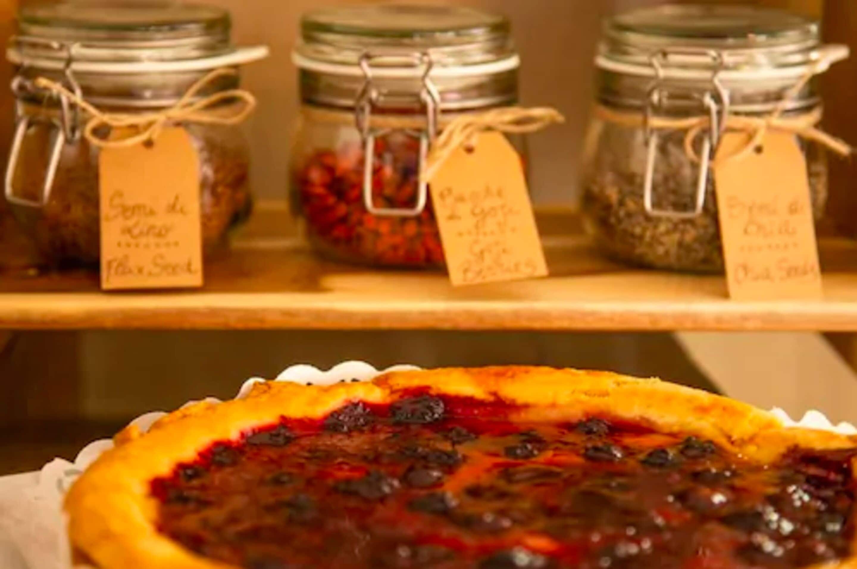 Three jars of preserves on a shelf with a pie in the foreground.